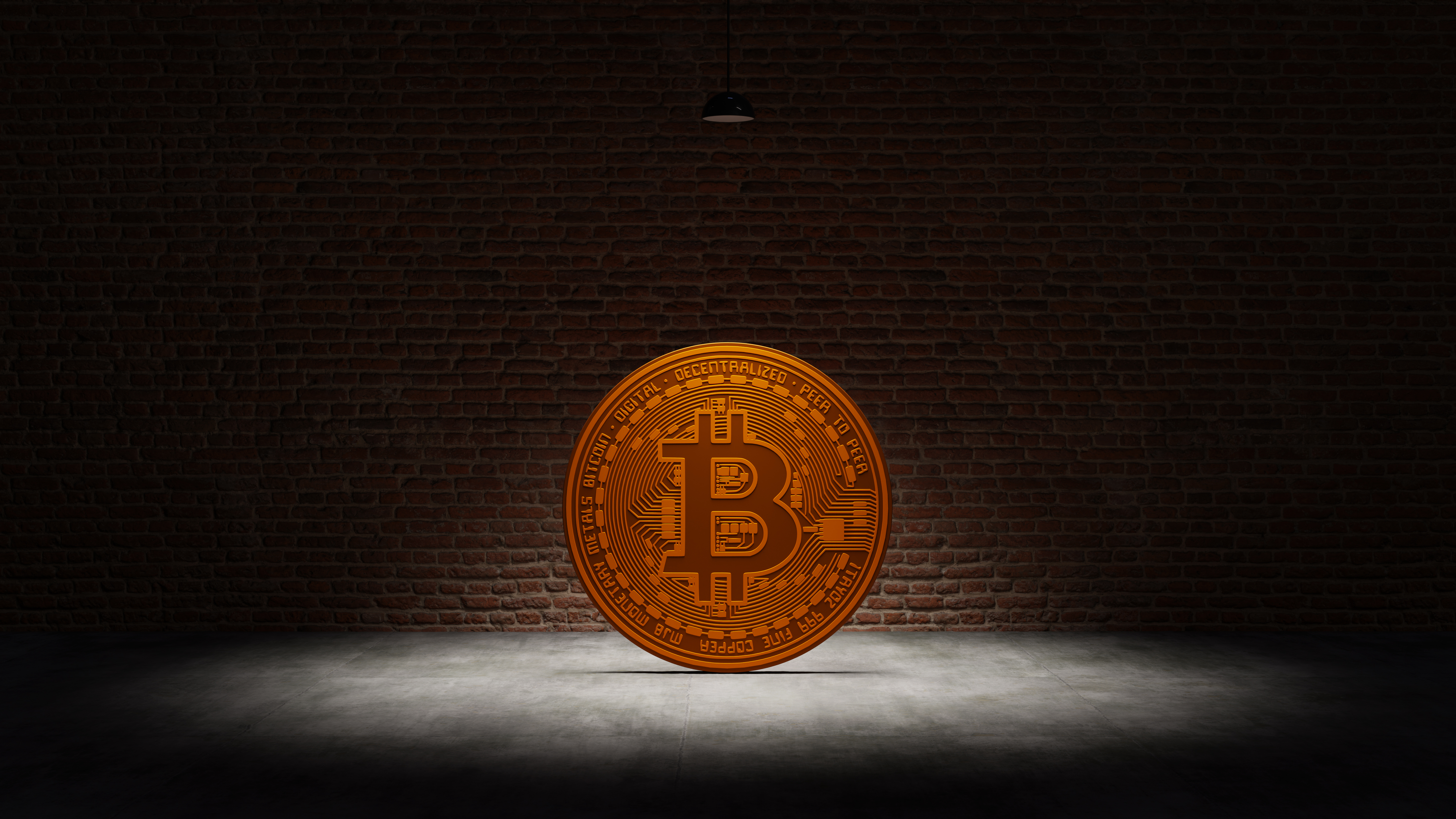 Golden Bitcoin under a white spotlight in front of a brick wall